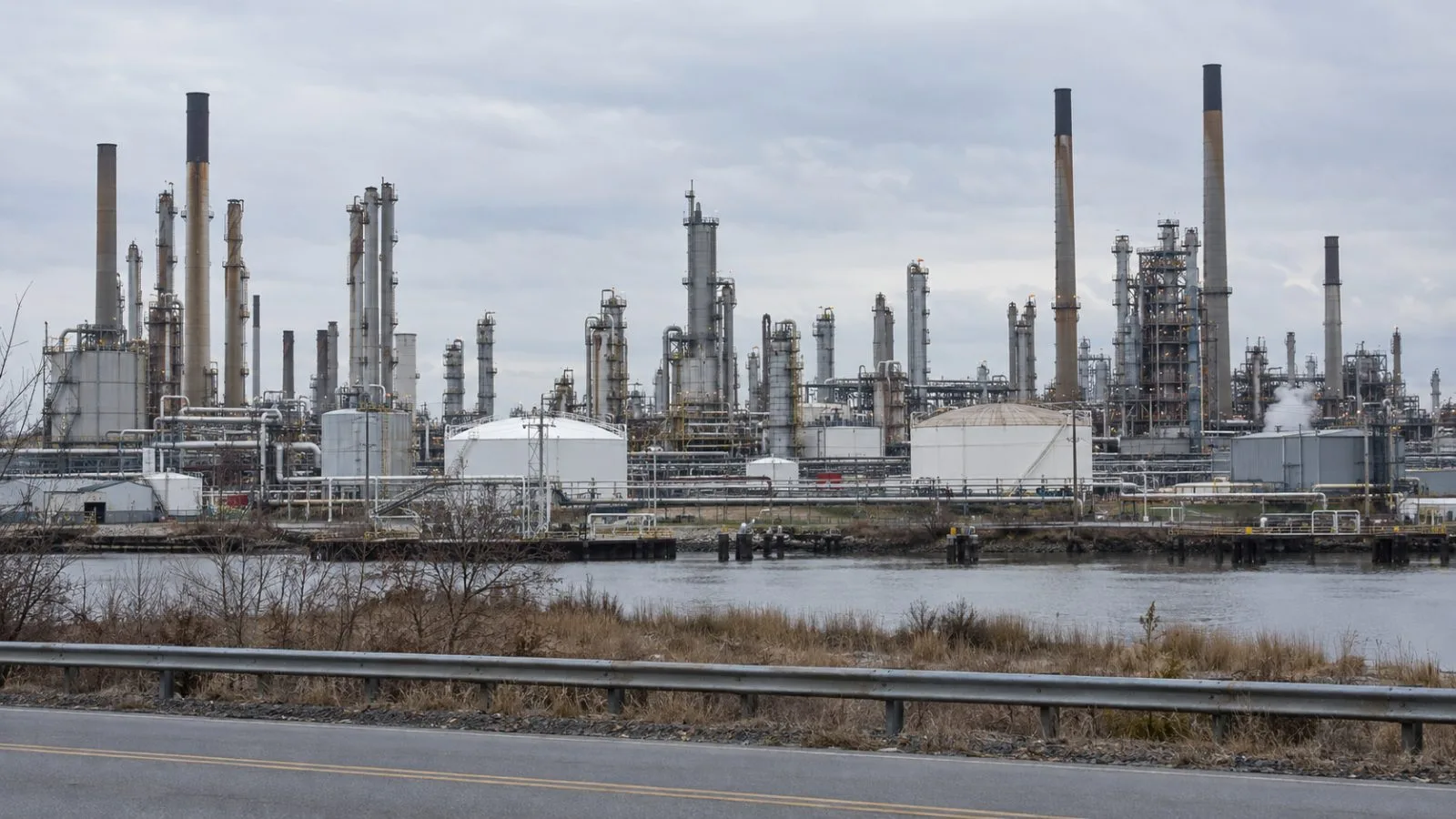 Refinery towers and pipework rise above the Delaware River near Delaware City, Delaware. (AI-generated image / EconoTimes)