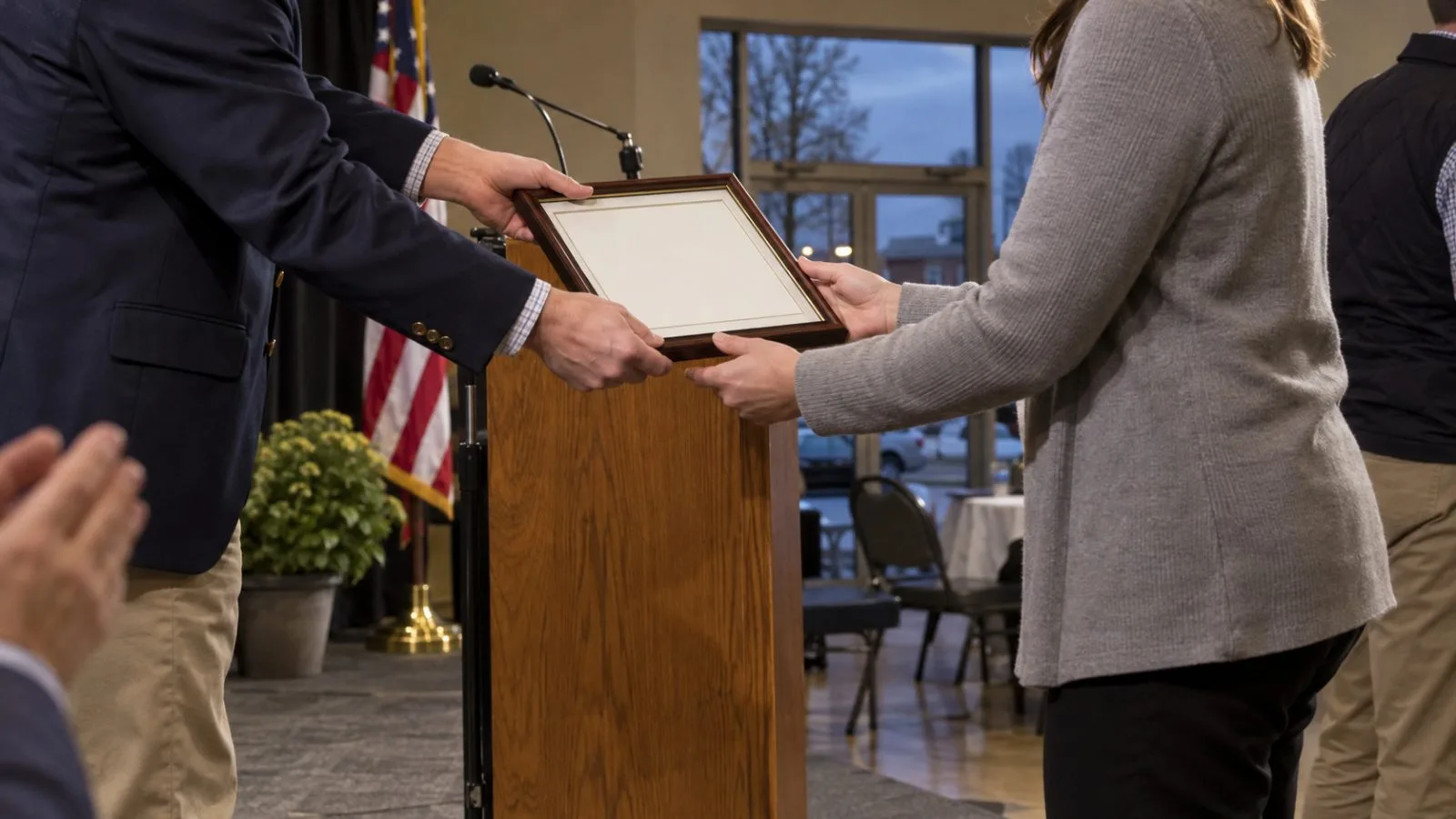 An aide receives a framed certificate beside a campaign rally stage in Sioux City, Iowa. (AI-generated image / EconoTimes)