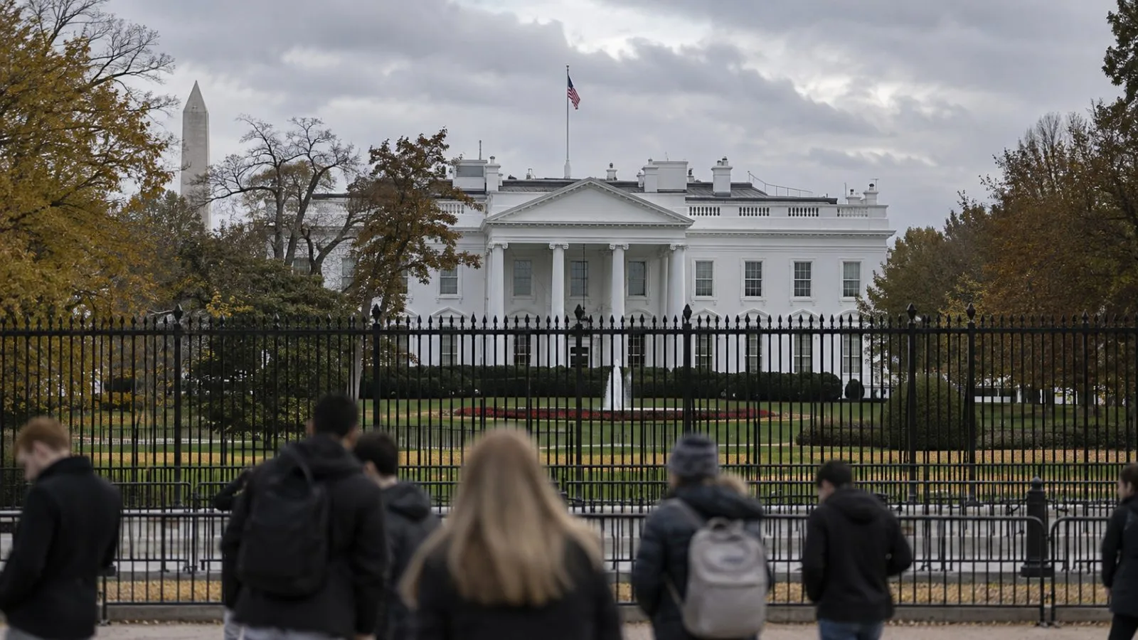 Pedestrians pass the White House perimeter fence under overcast skies in Washington. (AI-generated image / EconoTimes)