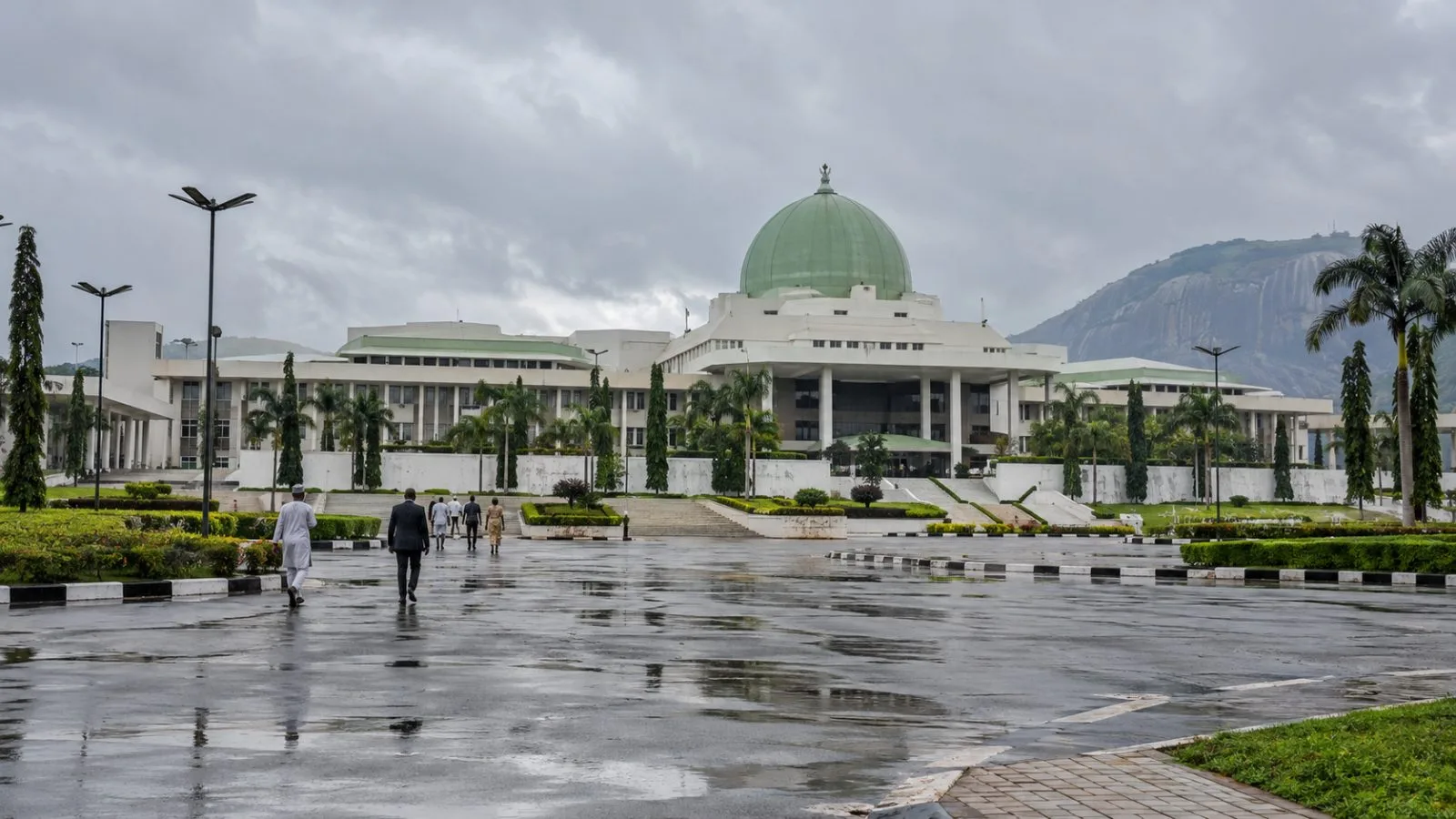 Visitors walk past the National Assembly complex in Abuja, Nigeria, on an overcast afternoon. (AI-generated image / EconoTimes)