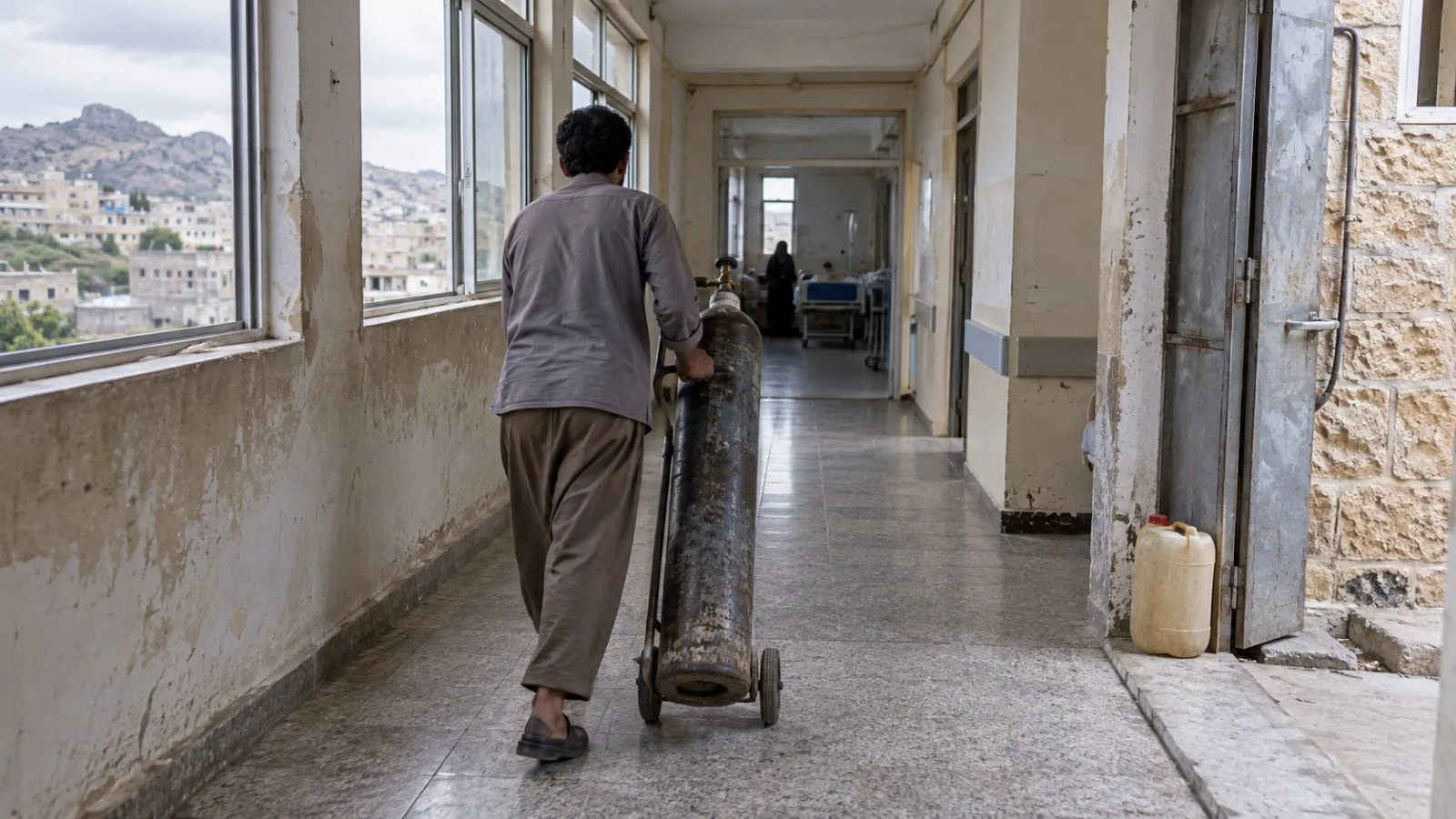An oxygen cylinder stands in a Taiz hospital corridor as a worker moves supplies amid shortages (AI-generated image / EconoTimes)