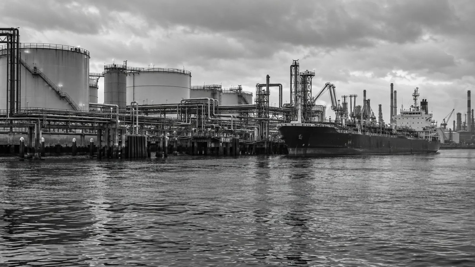 Storage tanks and pipeline gantries stand beside a cargo vessel at the Port of Rotterdam, Netherlands. (AI-generated image / EconoTimes)