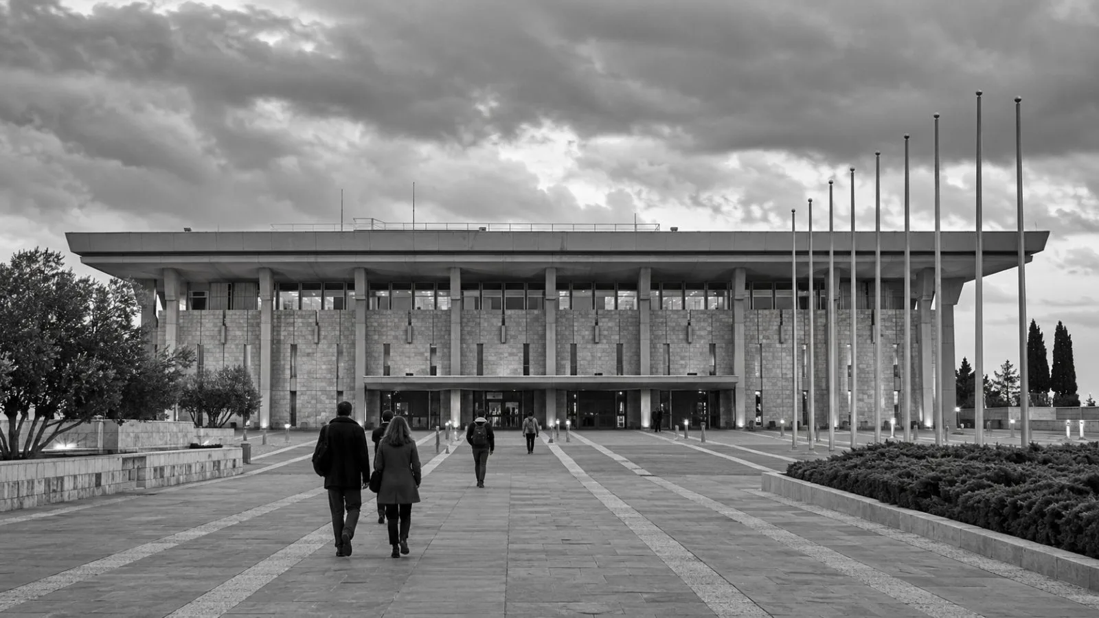 Visitors walk toward the Knesset entrance in Jerusalem beneath a cloudy afternoon sky. (AI-generated image / EconoTimes)