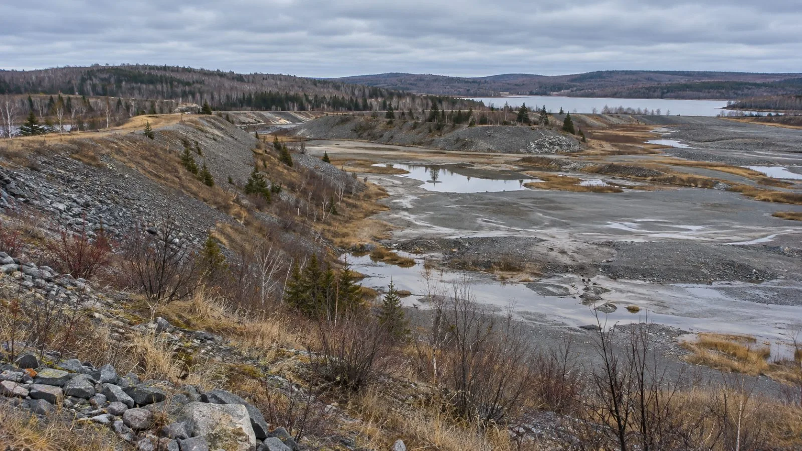 Weathered tailings embankments mark the former Nigadoo mine in Nigadoo, New Brunswick. (AI-generated image / EconoTimes)