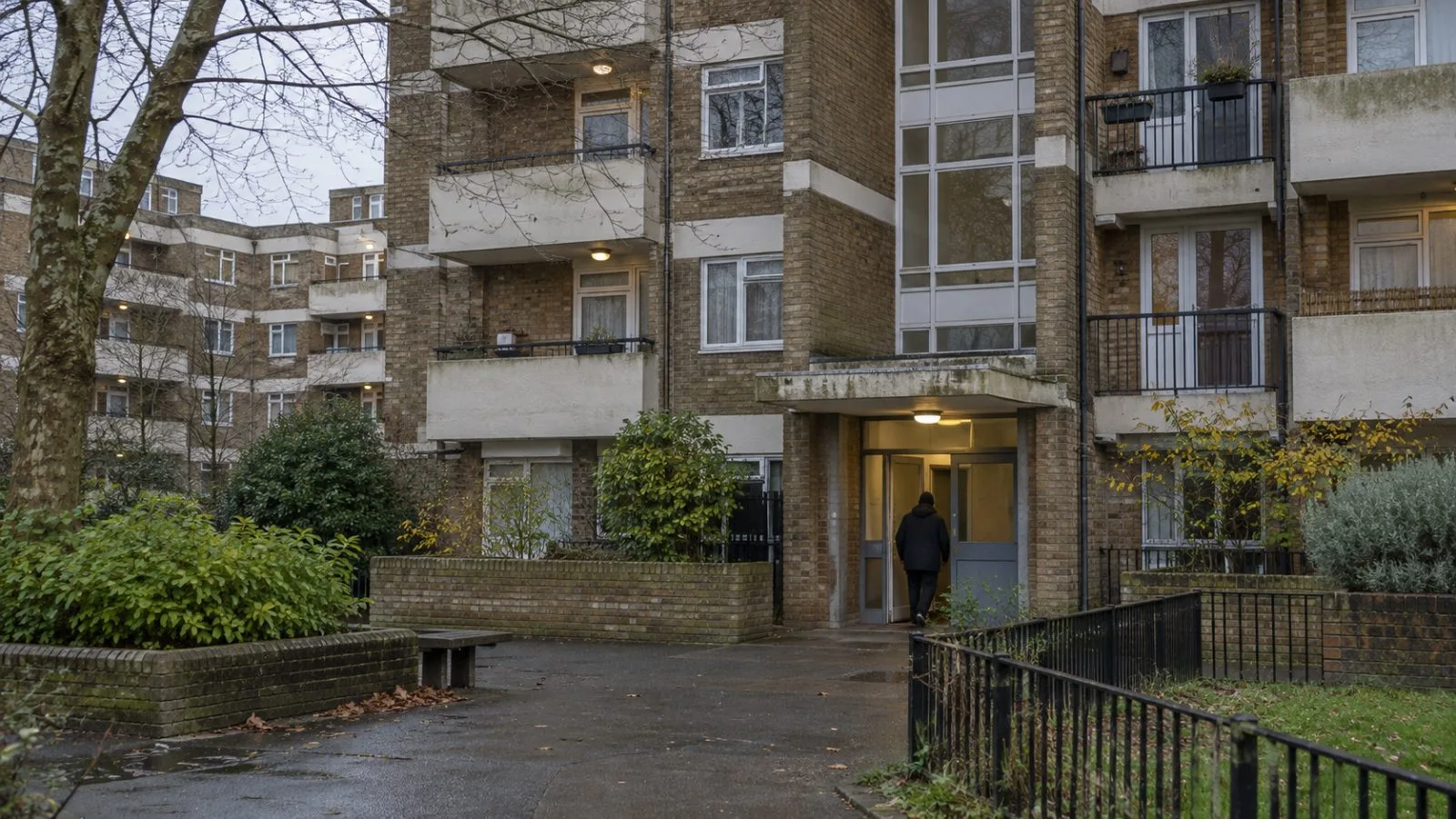 A resident enters a social housing block in London, England, on an overcast afternoon. (AI-generated image / EconoTimes)