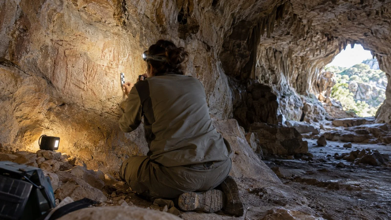 An archaeologist documents carved inscriptions on a cave wall inside Cova Dones near Millares, Spain. (AI-generated image / EconoTimes)