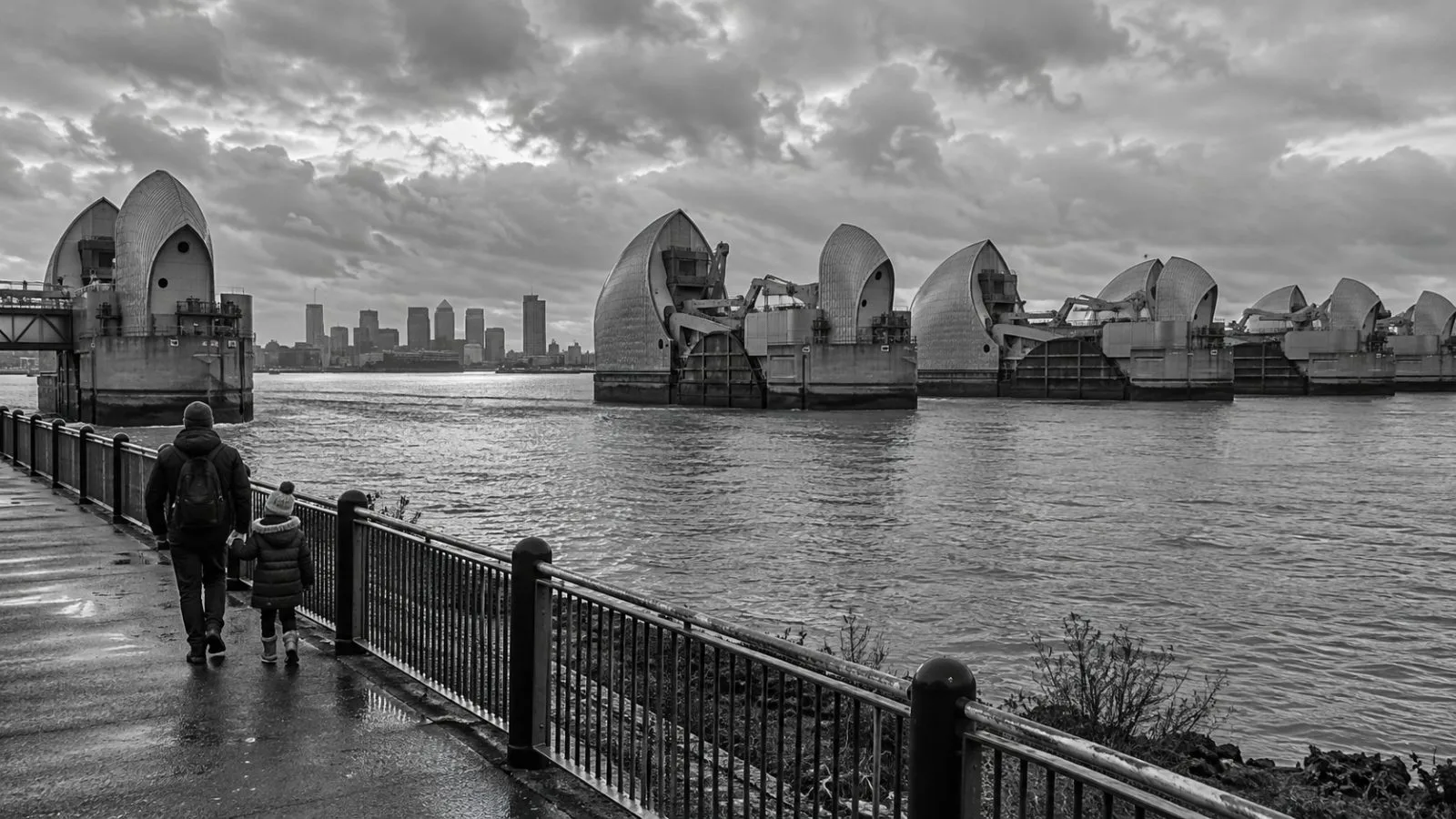 The Thames Barrier spans the River Thames in London as a child and adult walk along the riverside path (AI-generated image / EconoTimes)