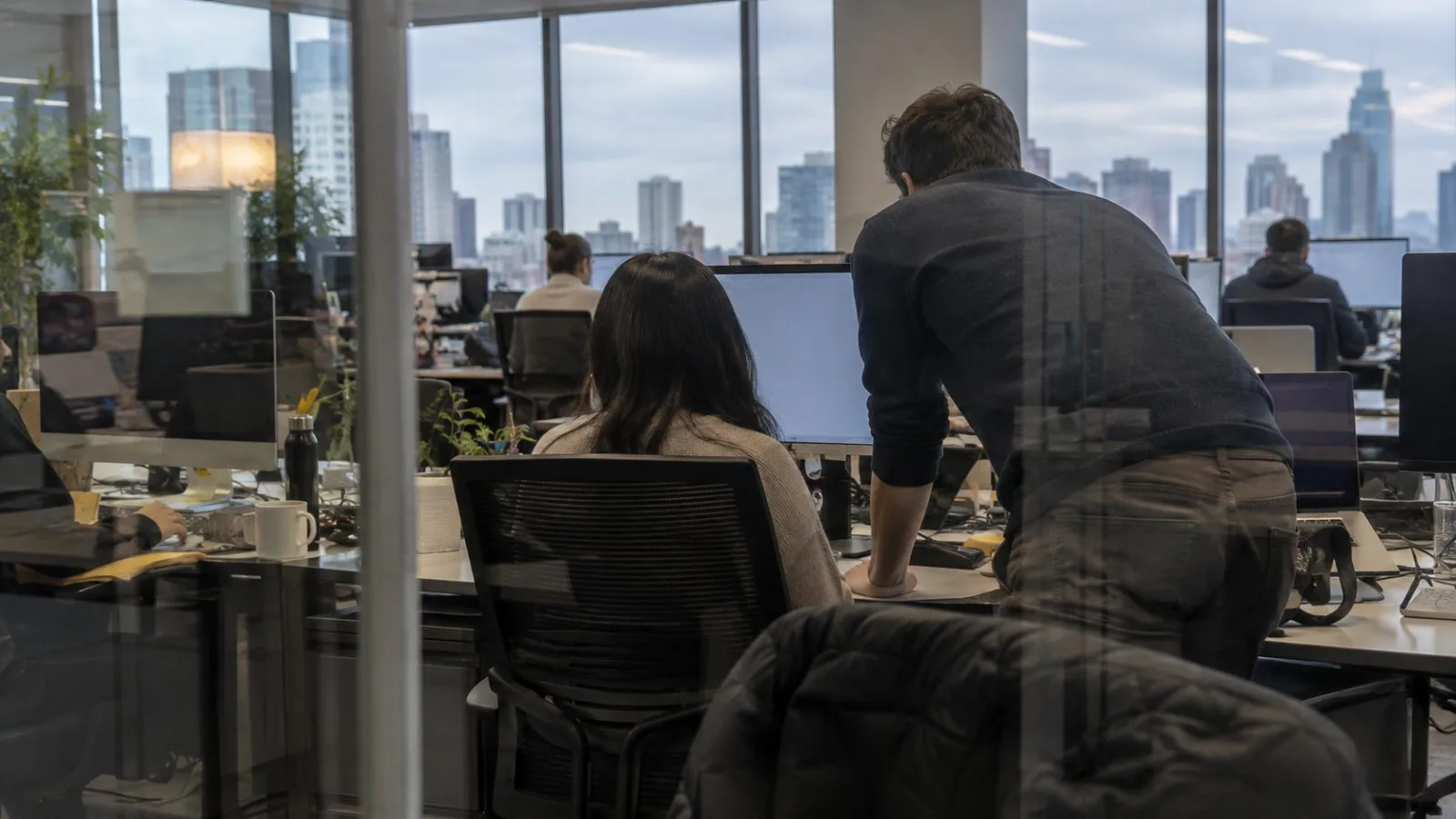 A worker reviews a colleague's computer screen in a Chicago office. (AI-generated image / EconoTimes)