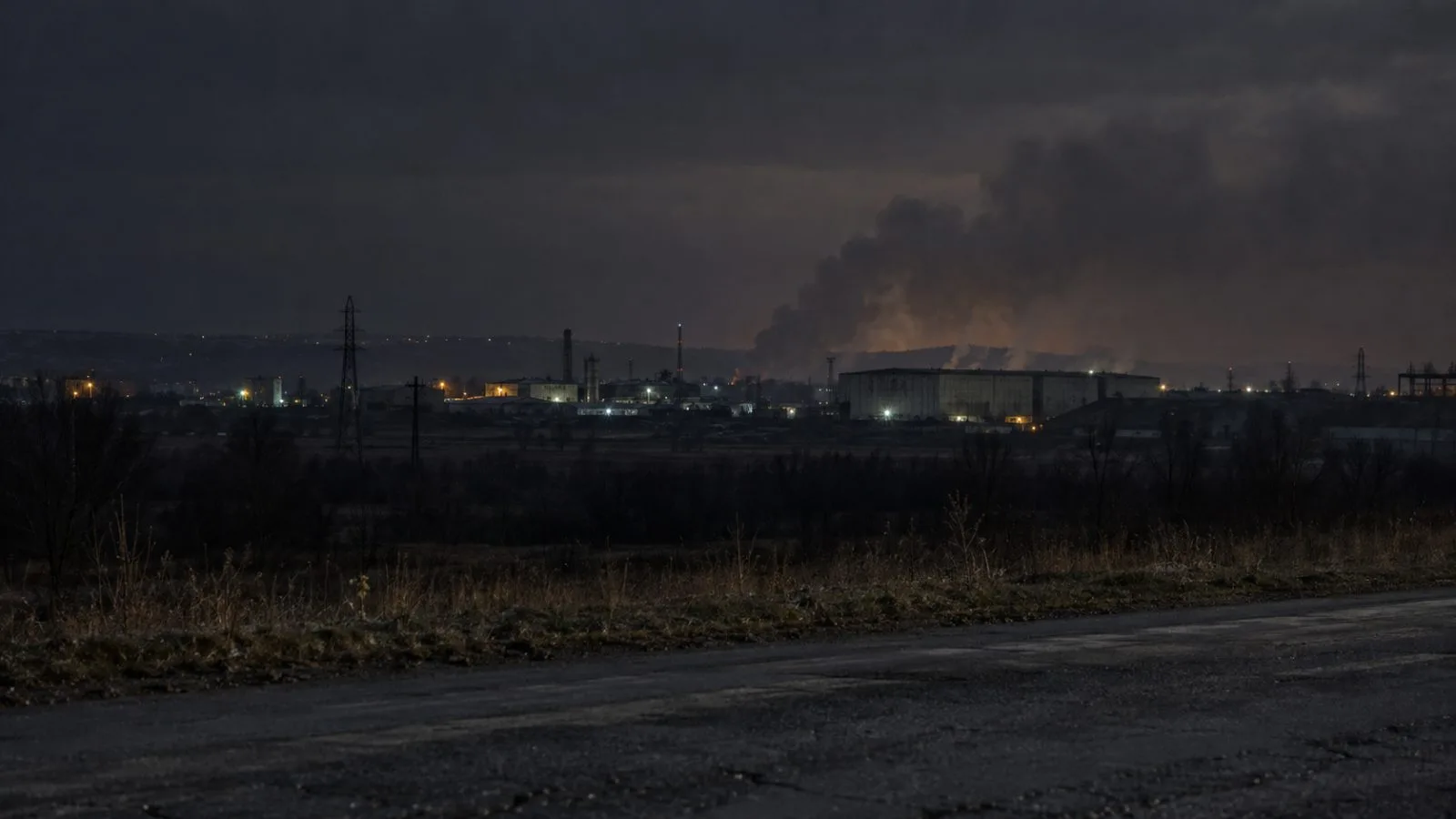 Smoke hangs above industrial buildings outside Khrustalnyi, Ukraine, beneath a dark overcast sky. (AI-generated image / EconoTimes)