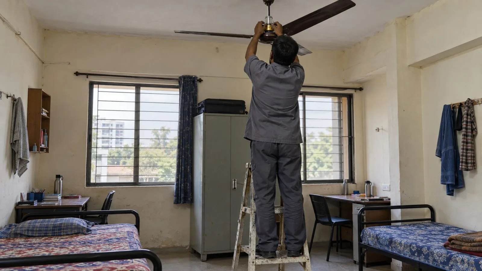 A worker installs a safety mechanism on a ceiling fan in a Surat hostel room. (AI-generated image / EconoTimes)