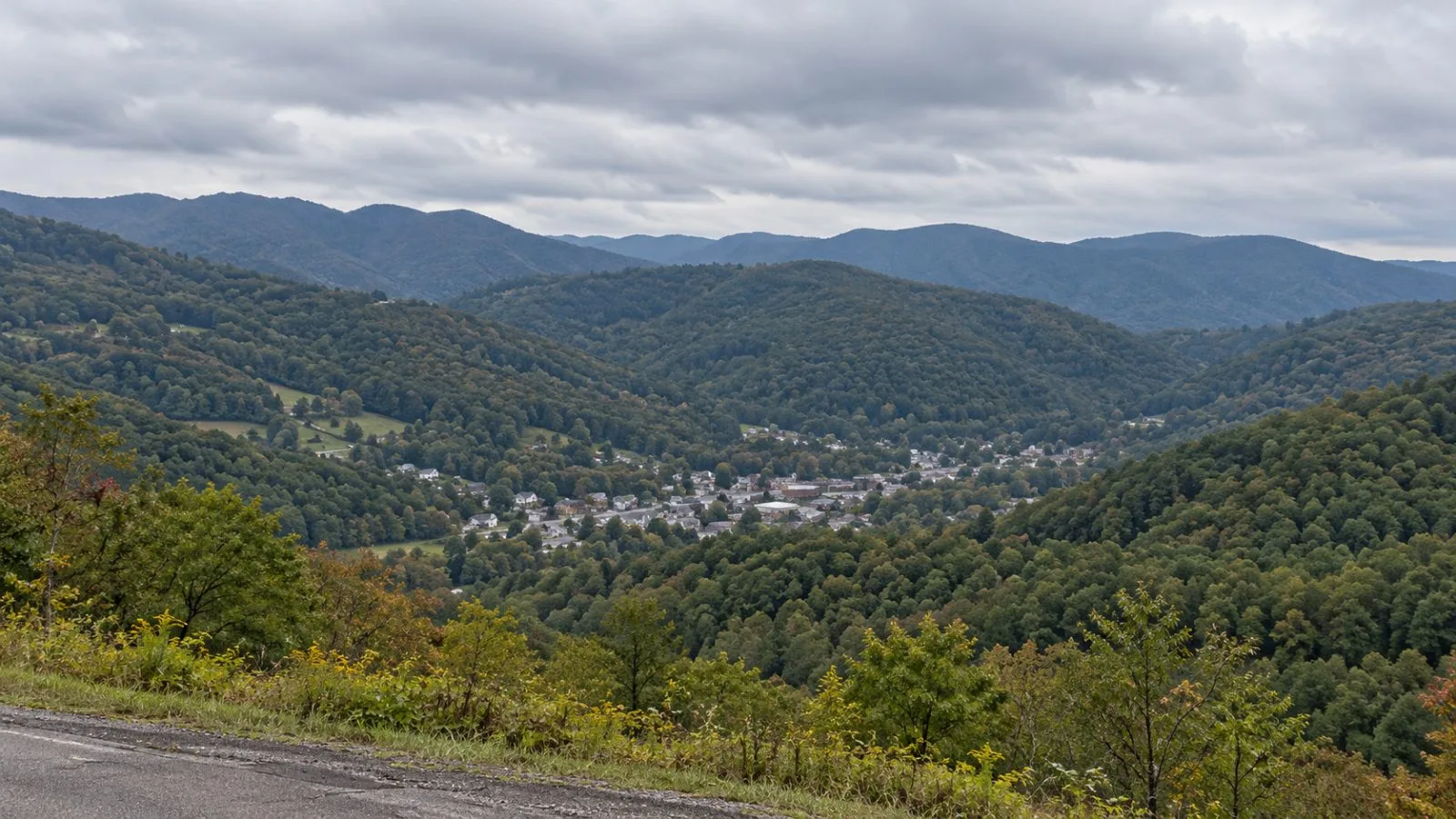A forested mountain ridge rises beyond a roadside near Thomas, West Virginia. / EconoTimes.ai