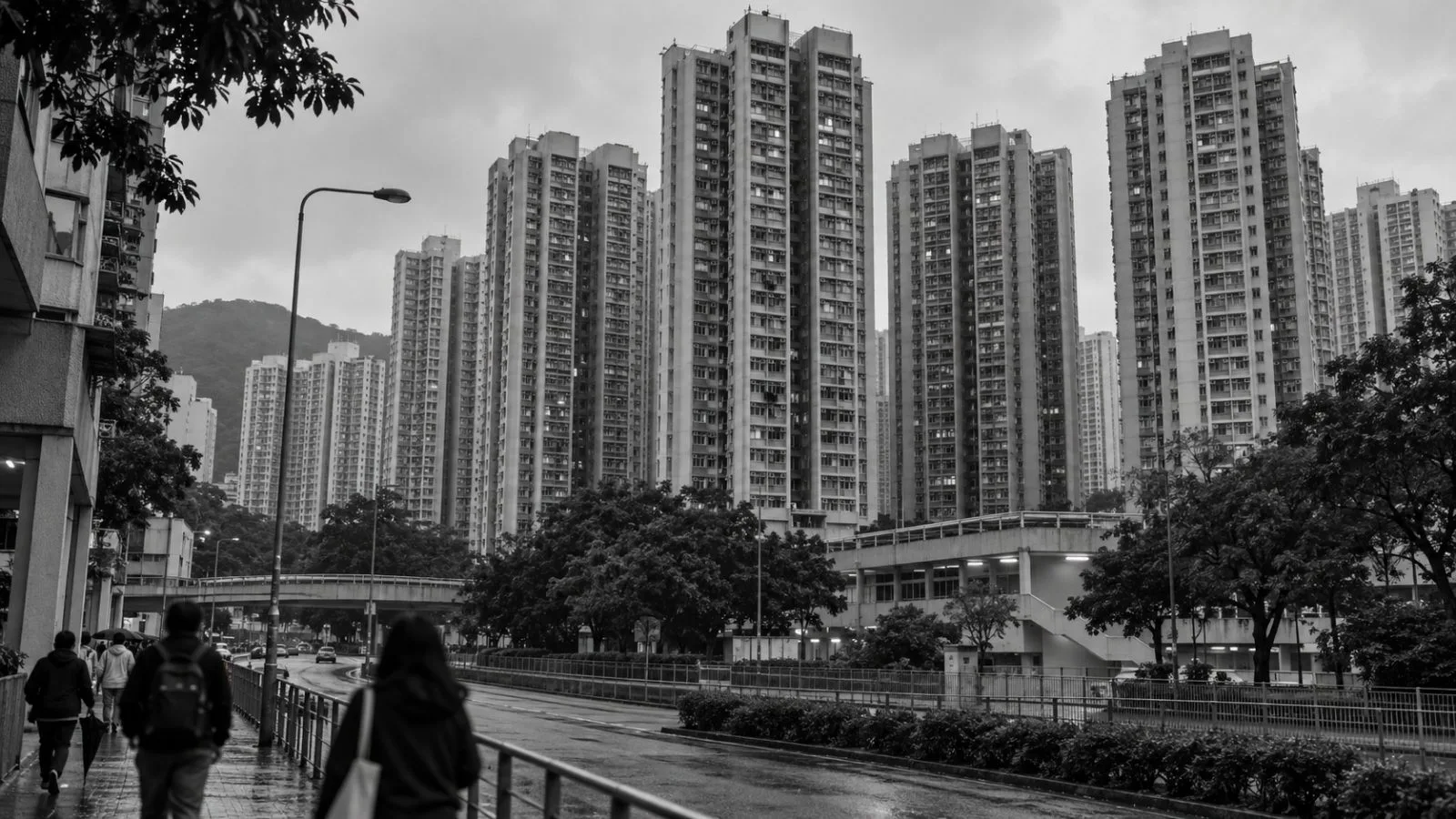 Fire-damaged residential towers stand behind a cordon at Wang Fuk Court in Tai Po, Hong Kong. / EconoTimes.ai (mono)