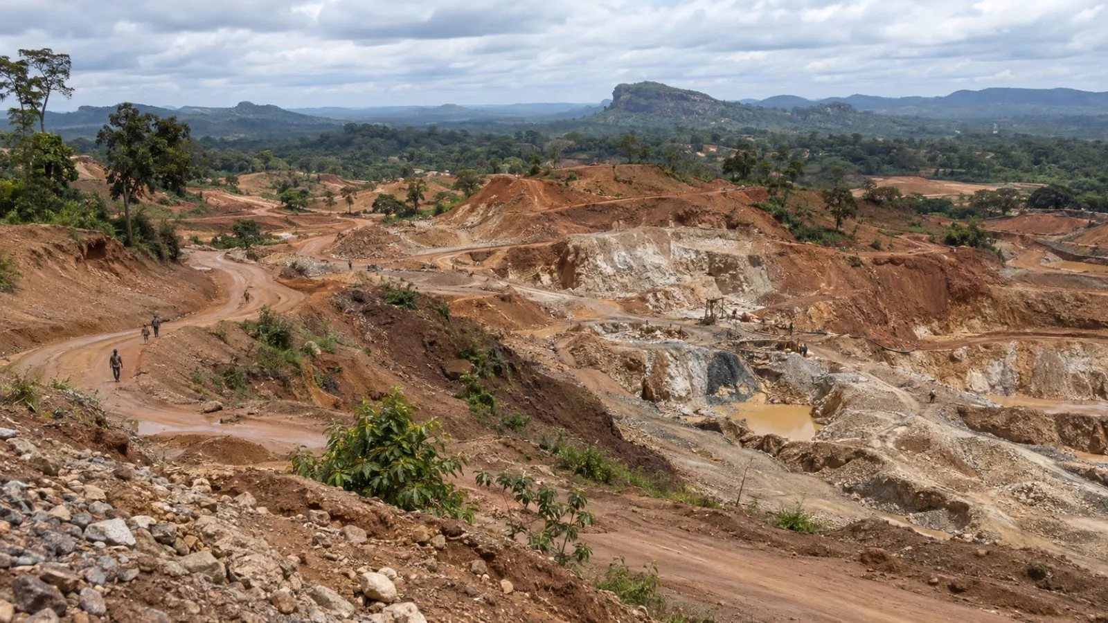 Excavated slopes border a dirt road at the Ndassima gold mine near Bambari. (AI-generated image / EconoTimes)