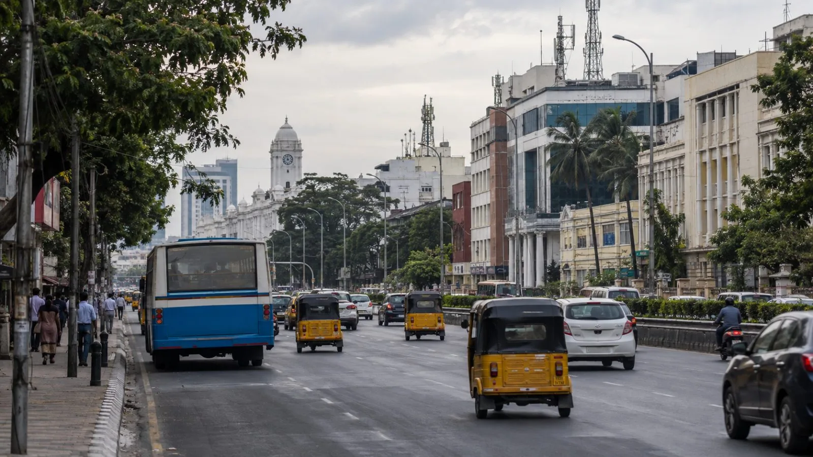 A city bus and auto-rickshaws move through light haze on Anna Salai in Chennai, India. (AI-generated image / EconoTimes)