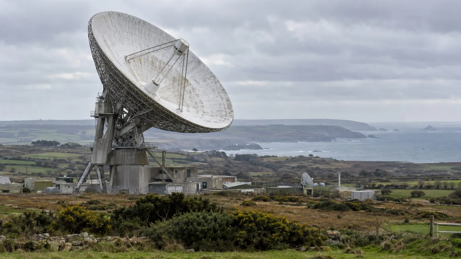 A satellite dish stands above the coastal landscape at Goonhilly Earth Station in Cornwall. (AI-generated image / EconoTimes)