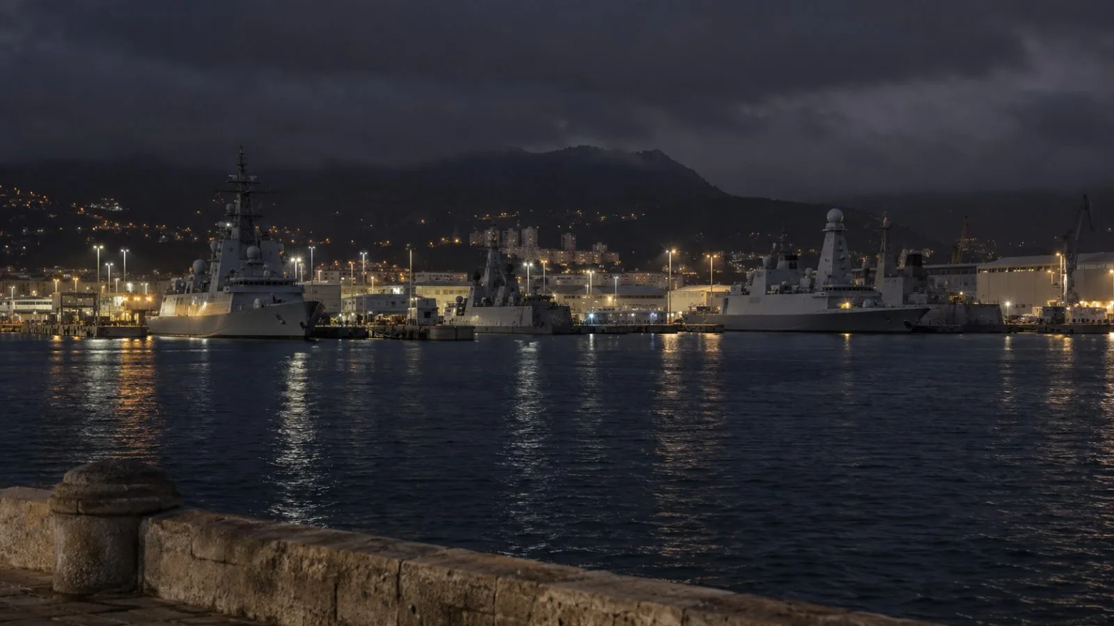 Harbor lights illuminate docked military vessels at the Toulon naval base in France. (AI-generated image / EconoTimes)