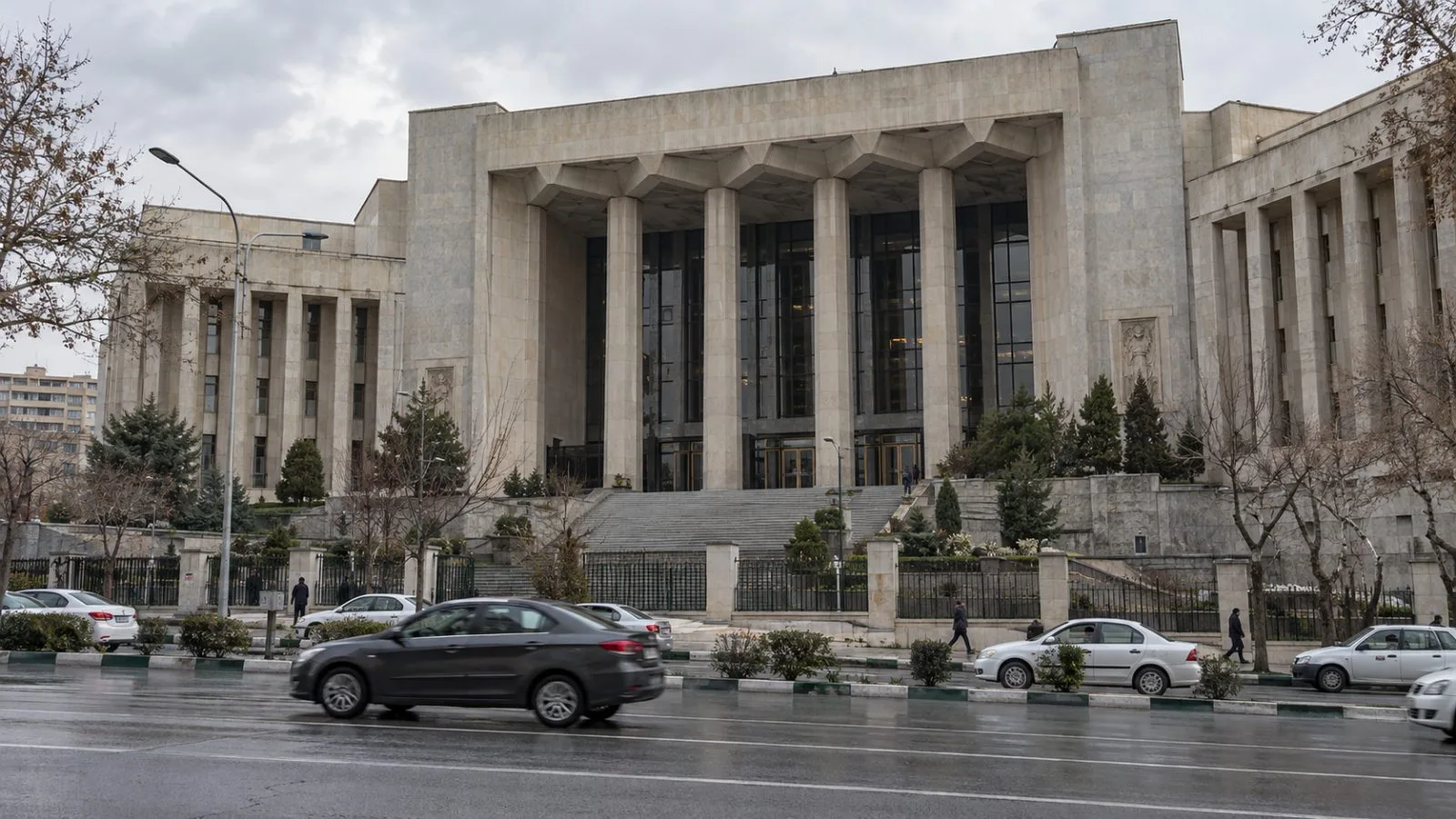 Iran’s parliament building stands beside a Tehran street under overcast afternoon light (AI-generated image / EconoTimes)