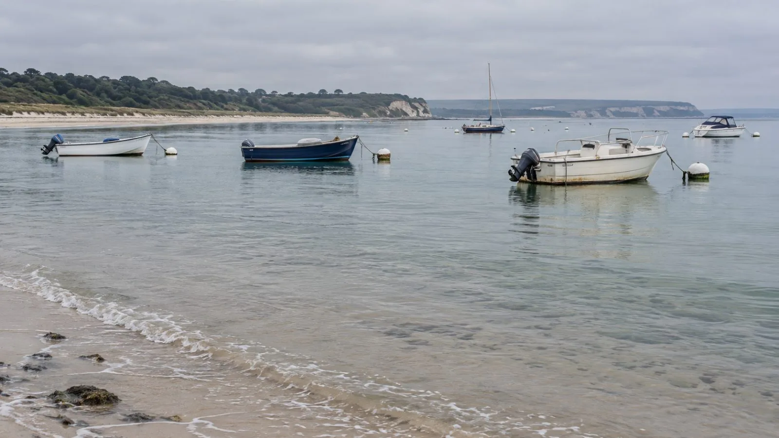 Small boats sit beside mooring buoys in Studland Bay, Dorset, England. (AI-generated image / EconoTimes)