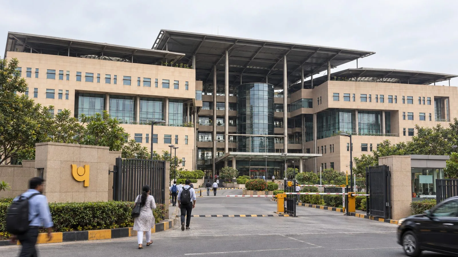 Commuters pass the entrance to a bank headquarters in Dwarka, New Delhi, India. / EconoTimes.ai