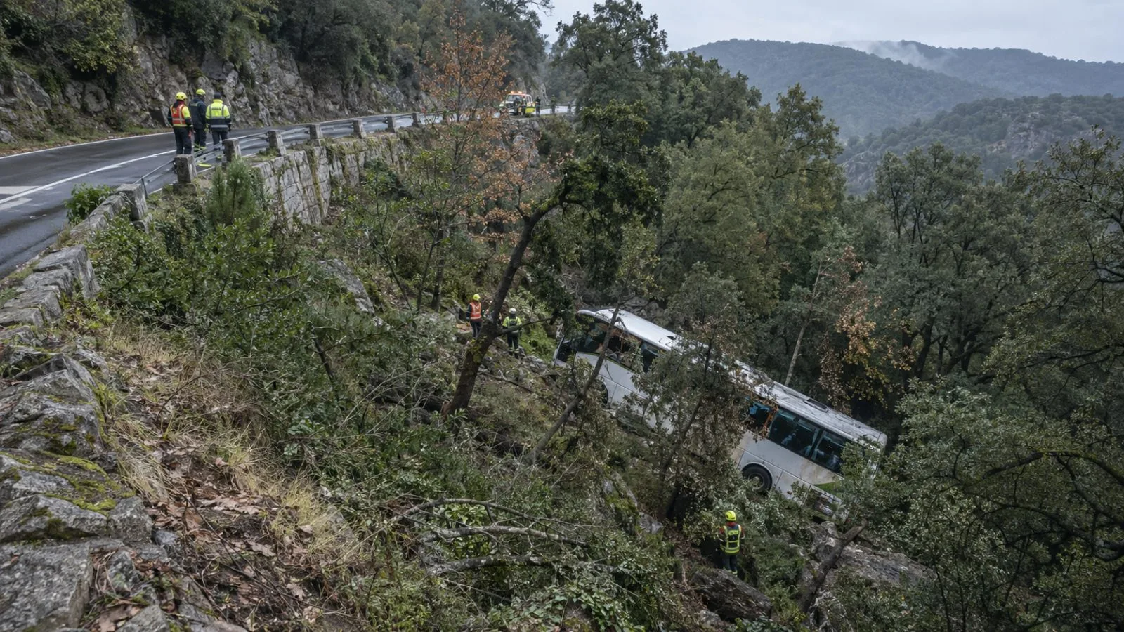 Rescue workers inspect a passenger bus below a winding road near Fogars de Montclús, Spain. (AI-generated image / EconoTimes)