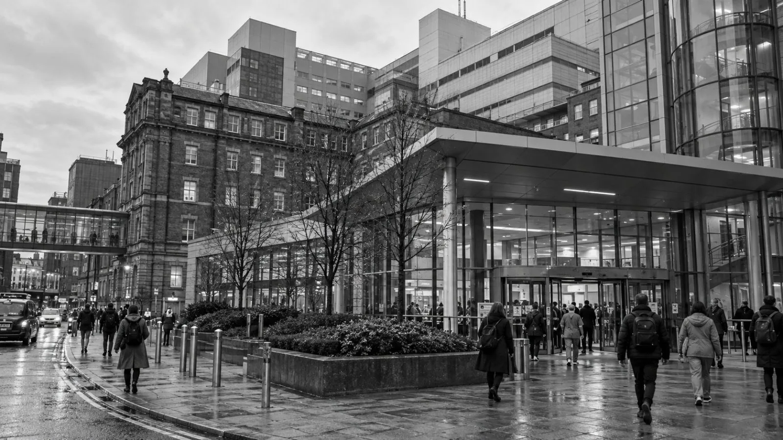 Adults pass the entrance to Manchester Royal Infirmary in Manchester, England, on an overcast morning. (AI-generated image / EconoTimes)