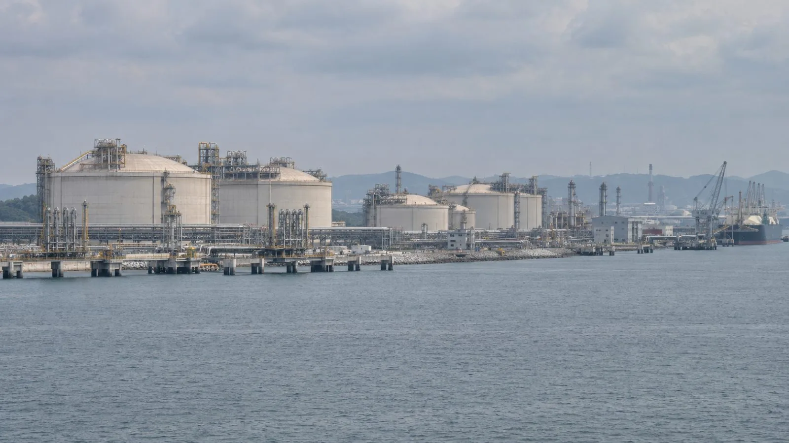 LNG storage tanks stand beside the waterfront at Map Ta Phut in Rayong, Thailand. (AI-generated image / EconoTimes)