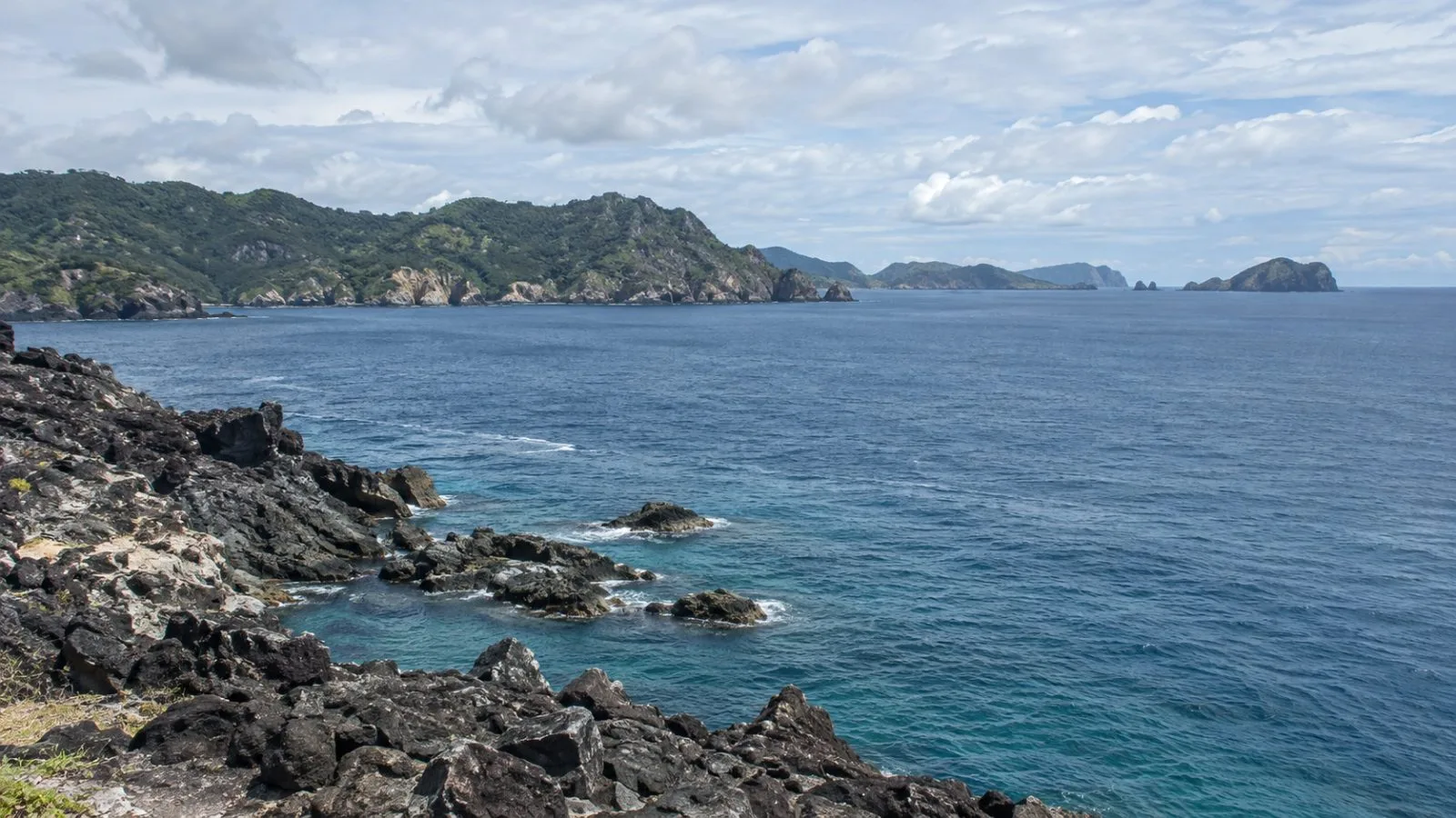 Open water lies beyond the rocky shore of Chichijima in Japan’s Bonin Islands. (AI-generated image / EconoTimes)